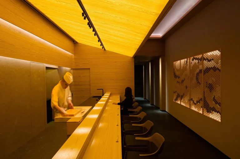 A man is at the Sushi Hare restaurant counter, interacting with the customer.