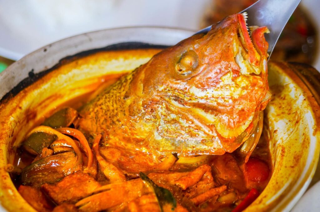 A large fish being cooked in a pot, showcasing the preparation of Fish Head Curry.