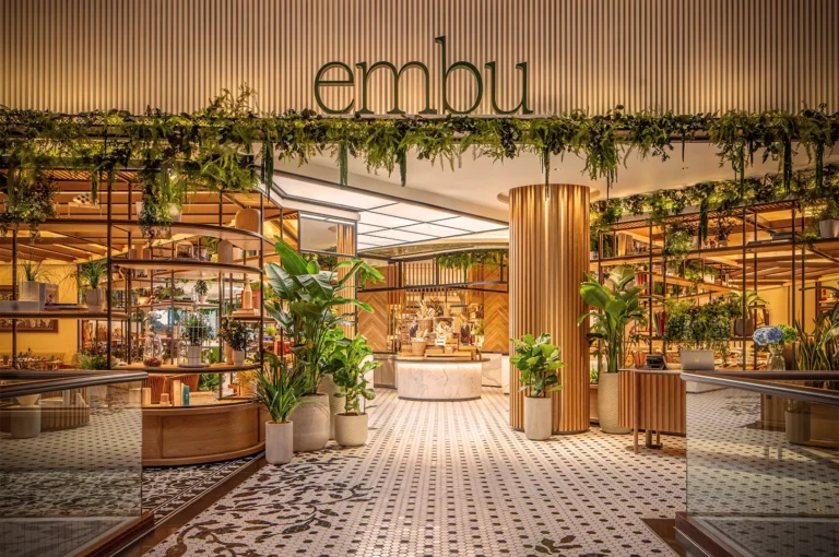 Entrance of Embu restaurant with lush greenery, modern wooden design, mosaic tile flooring, and inviting biophilic interior concept.