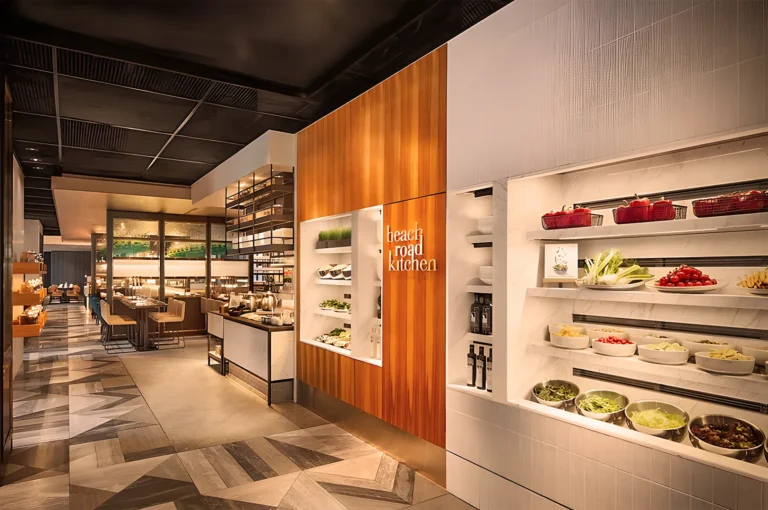 Modern restaurant interior with soft lighting, wooden accents, and a visible produce display. "Beach Road Kitchen" sign on wooden wall, creating a warm, inviting atmosphere.