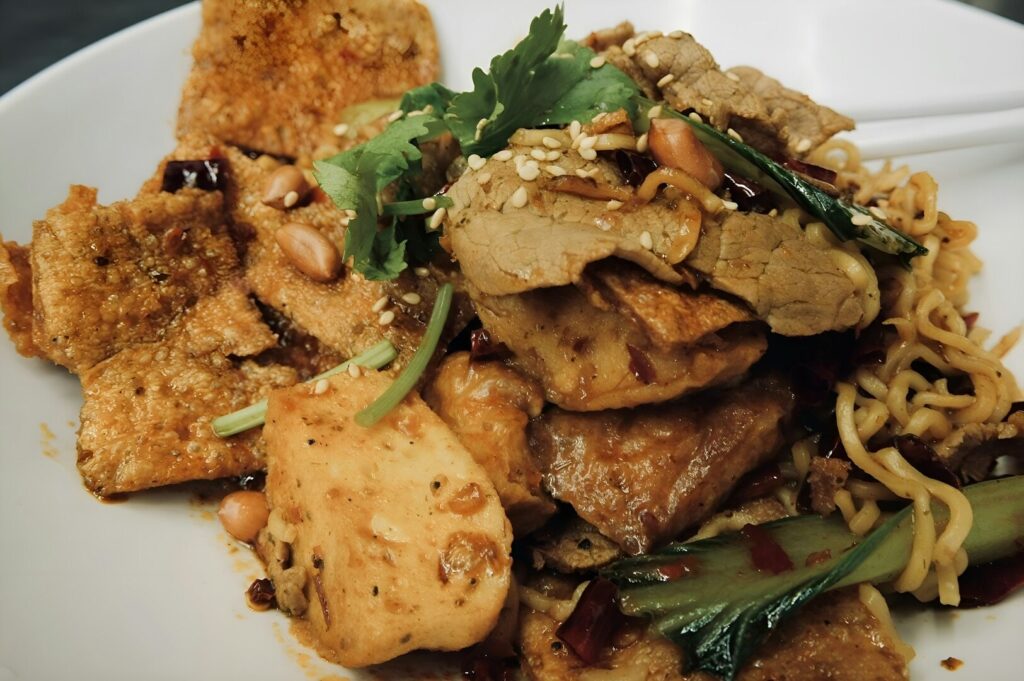 A plate of noodles topped with meat and vegetables, showcasing local dining in Singapore.