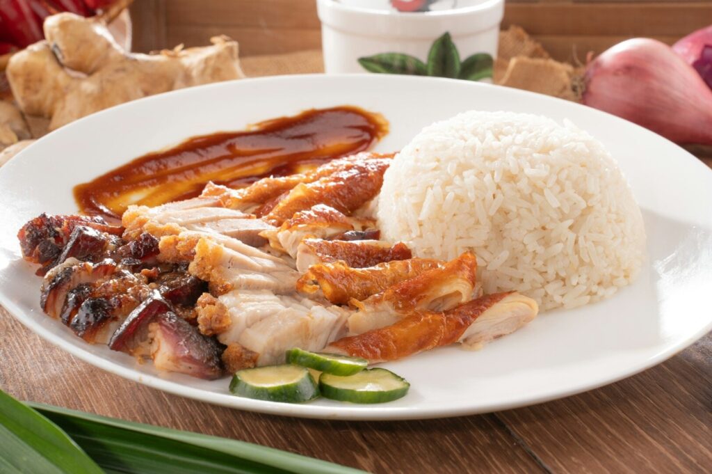 A plate of chicken rice featuring tender meat served over a bed of fluffy white rice, garnished with herbs.