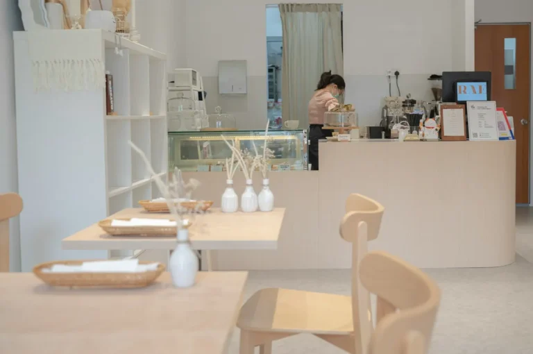 Bright minimalist cafe interior with light wood tables, white ceramic vases, and service counter with display case
