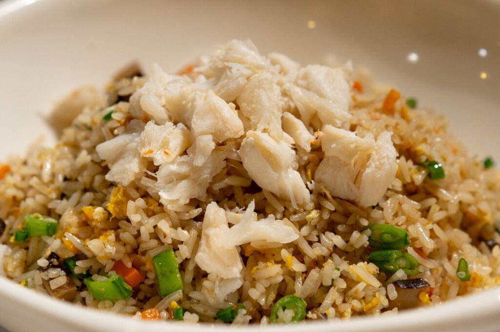 A bowl of Singapore Crab Fried Rice topped with meat and colorful vegetables.