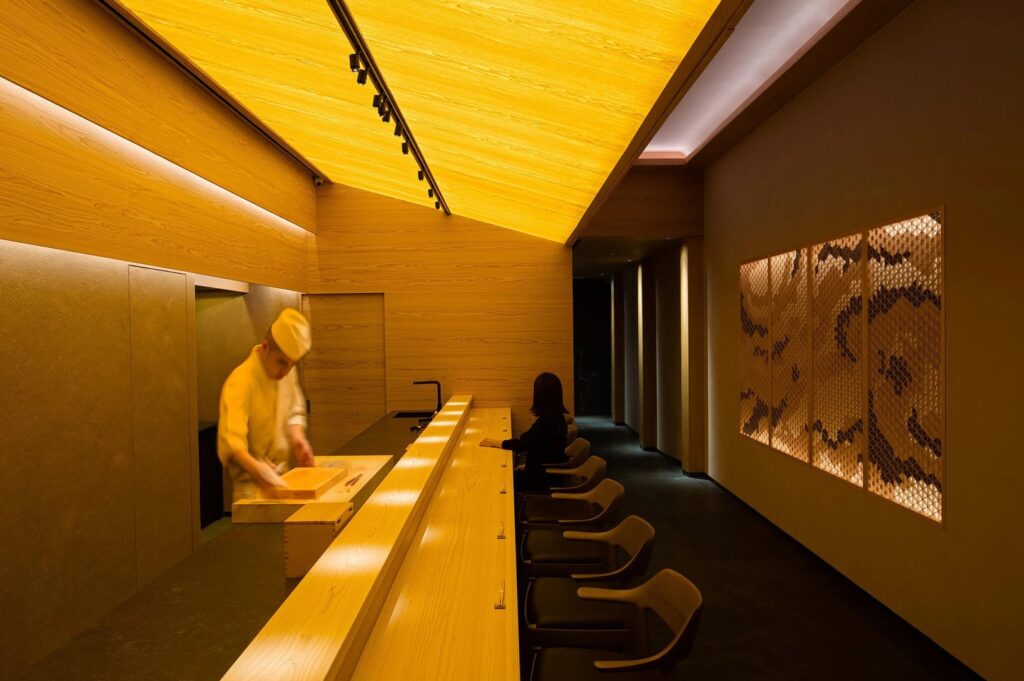 A man is at the Sushi Hare restaurant counter, interacting with the customer.