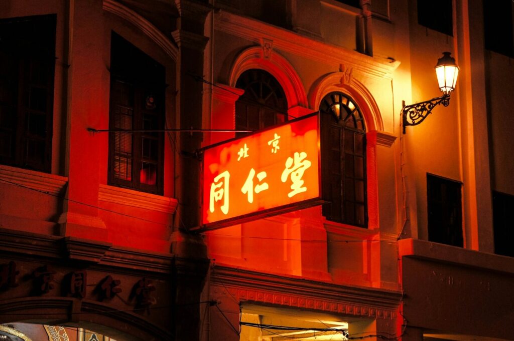 A vibrant red neon sign illuminates a Chinese restaurant building at night in Singapore.
