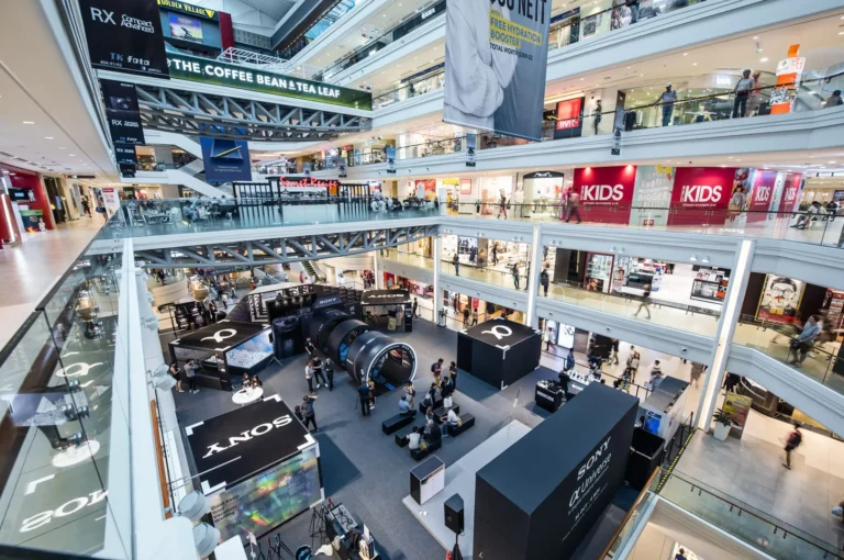 A bustling indoor shopping mall, Plaza Singapura, filled with shoppers walking and browsing various stores.