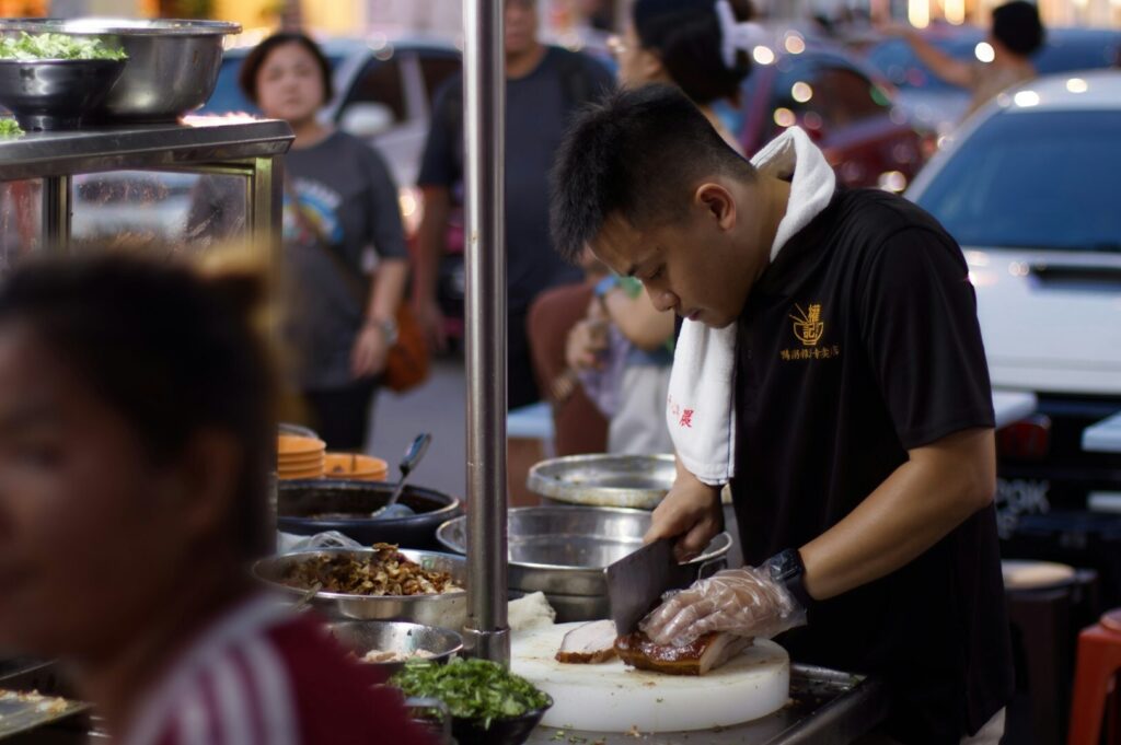 A street food vendor preparing dishes at his stand, showcasing colorful ingredients and a bustling atmosphere.
