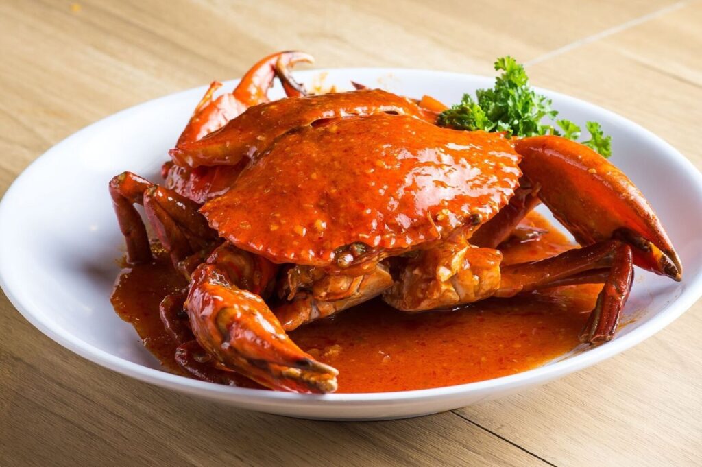 A crab sits on a plate, covered in rich chili sauce, showcasing a delicious Chili Crab dish.