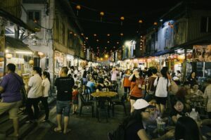 Crowded night scene at a Singapore hawker centre, with diners savoring meals and drinks in a lively atmosphere.
