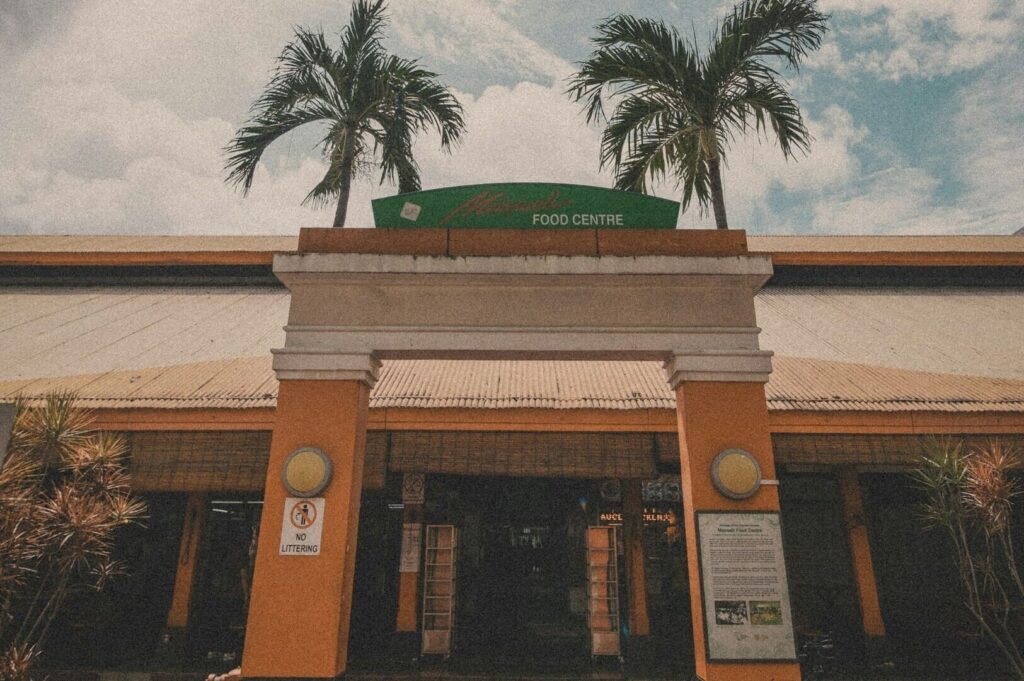 A restaurant in Singapore, the Maxwell Food Centre, featuring palm trees and a sign.
