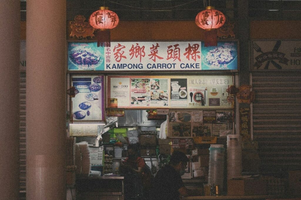 A man sits at a table outside a hawker stall serving Kampong Carrot Cake, enjoying his meal.