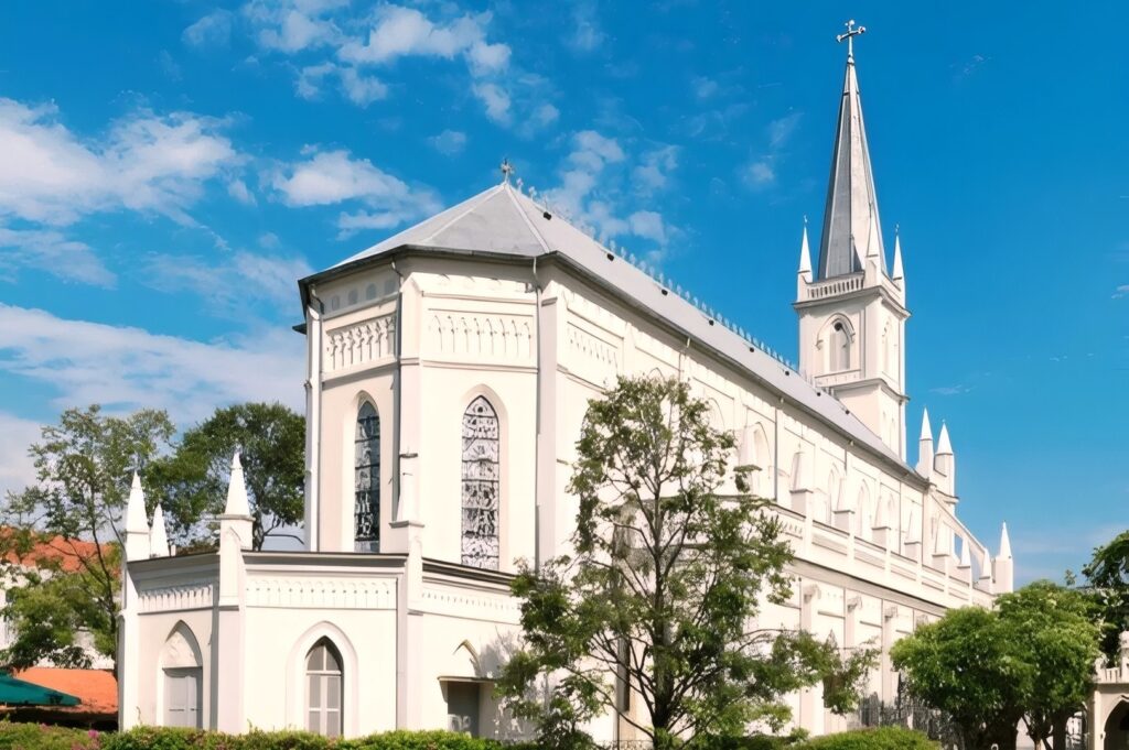 A historic white church, CHIJMES, surrounded by lush trees and bushes, showcasing beautiful architecture in Singapore.