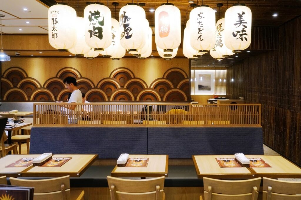 Restaurant seating area with tables and chairs in front of a large wall at Plaza Singapura.
