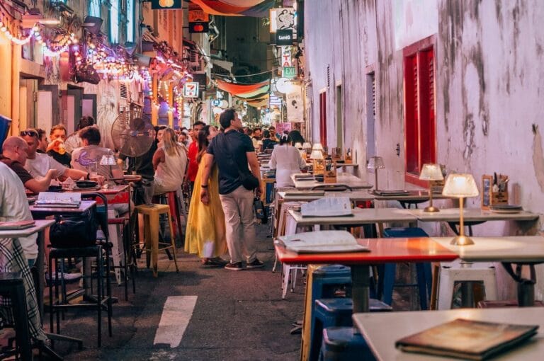 A narrow alley in Singapore featuring outdoor dining tables and chairs set up for guests.
