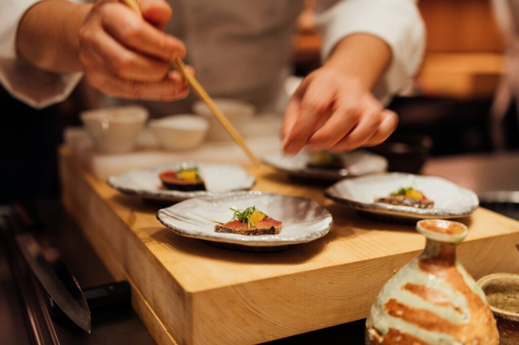 A chef is chopping fresh ingredients on a wooden cutting board, preparing for an Omakase dining experience.