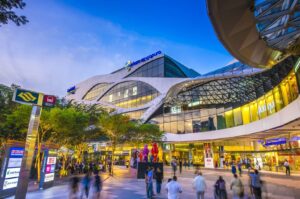 People walk in front of Plaza Singapura, a modern building in a bustling city setting.