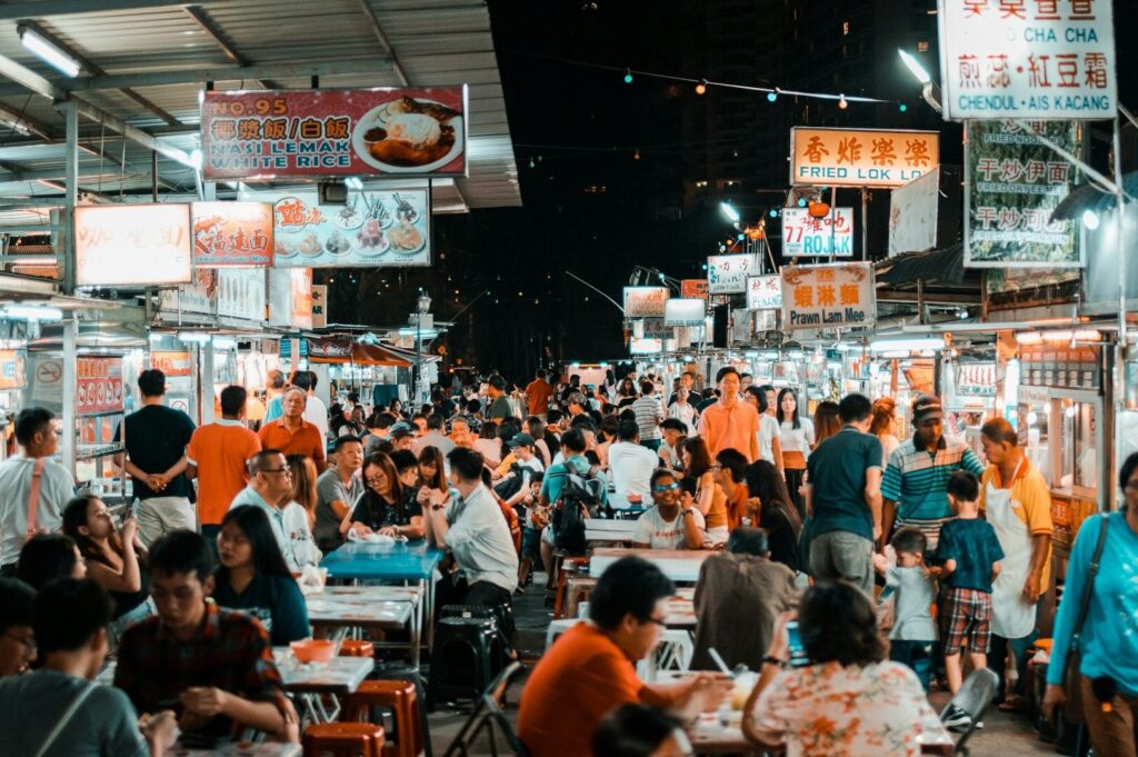 A bustling Singapore food market at night, filled with people enjoying various dishes and vibrant street food stalls.