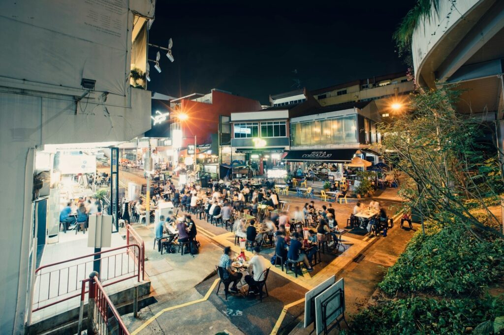 Crowded night scene at a Singapore hawker centre, with diners enjoying meals at outdoor tables.