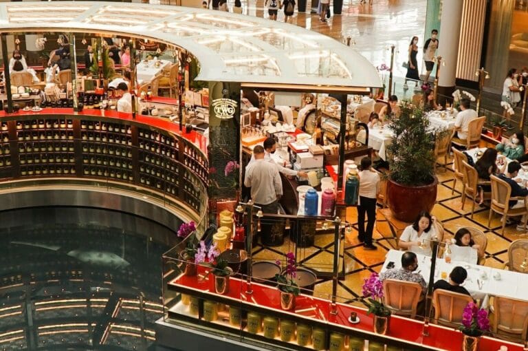 A vibrant indoor mall in Singapore, showcasing crowds of people eating and drinking at numerous dining establishments.