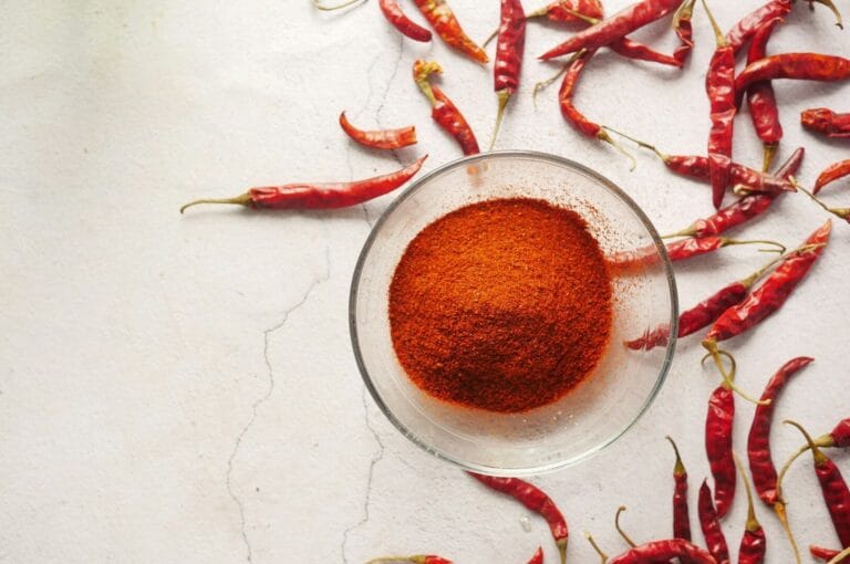 A bowl filled with chili powder on a white background, representing Peranakan Spices with its rich, red hue.