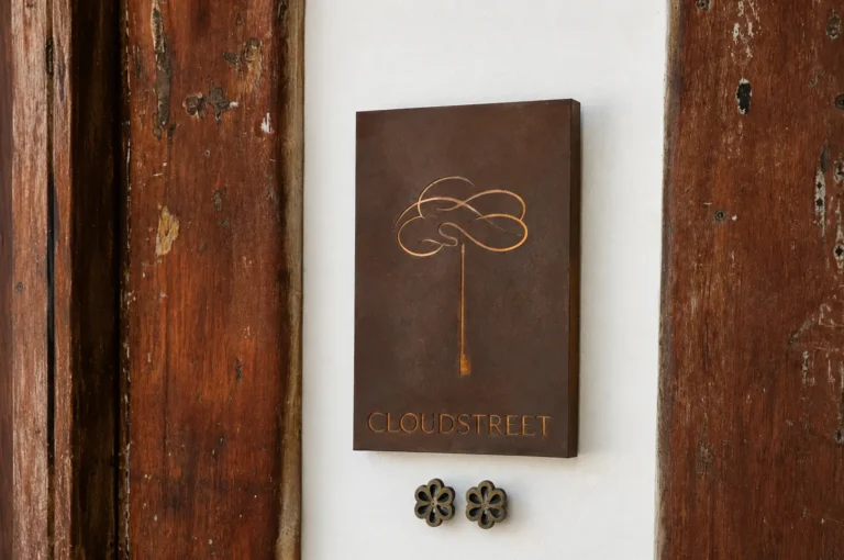 Rustic metal plaque with a tree logo and "Cloudstreet" text mounted on a white wall