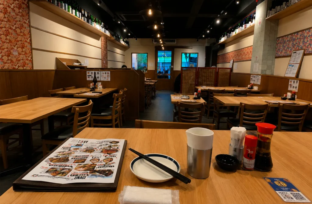 Wooden table set for dining at a Singapore izakaya with a menu, condiments, and shelves of bottles in the background