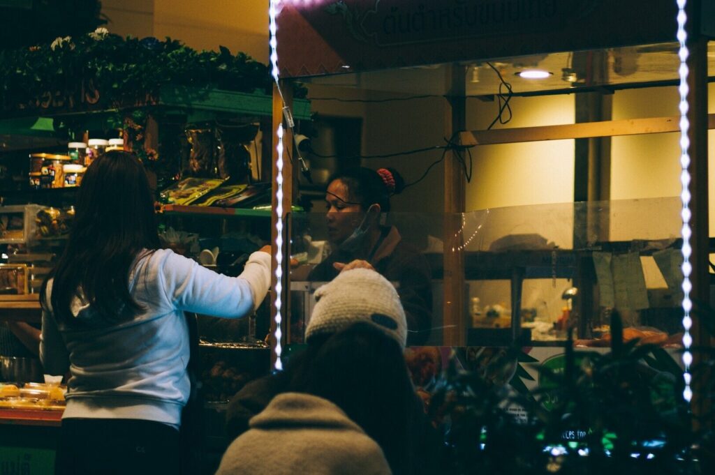 A woman in front of a counter at a Singapore restaurant, surrounded by a lively dining scene and colorful decor.