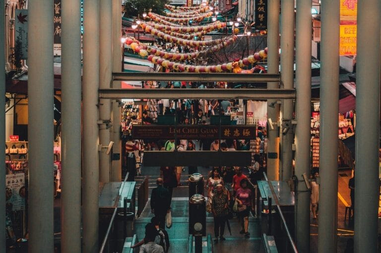 A bustling shopping mall in Chinatown, Singapore, filled with people walking and exploring various shops and stalls.