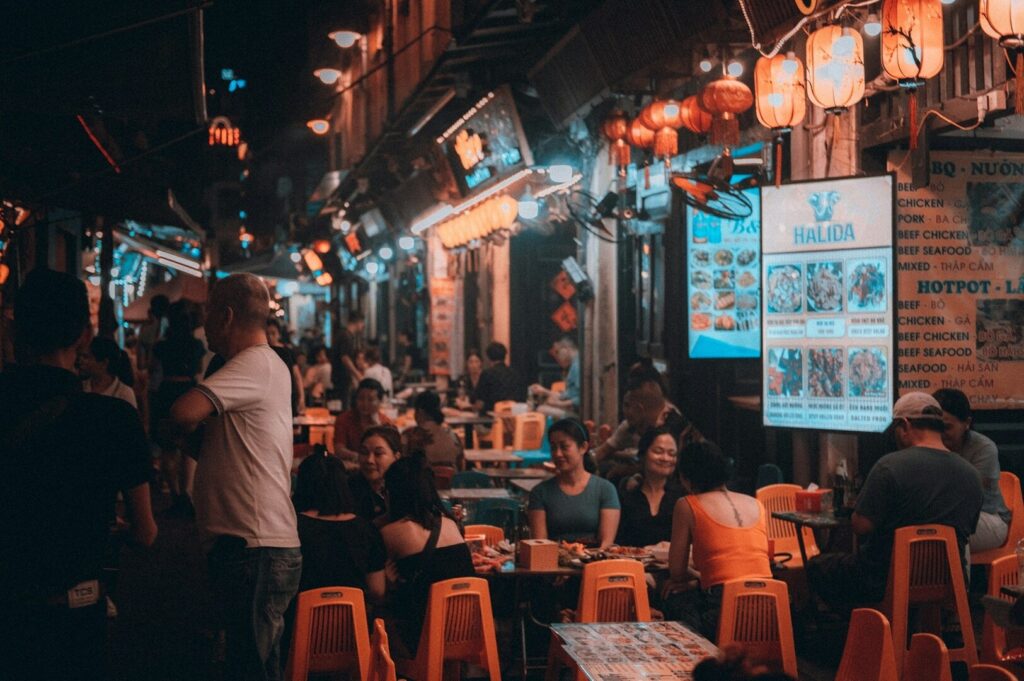 A bustling Singapore street at night, filled with people dining at tables under warm lights.