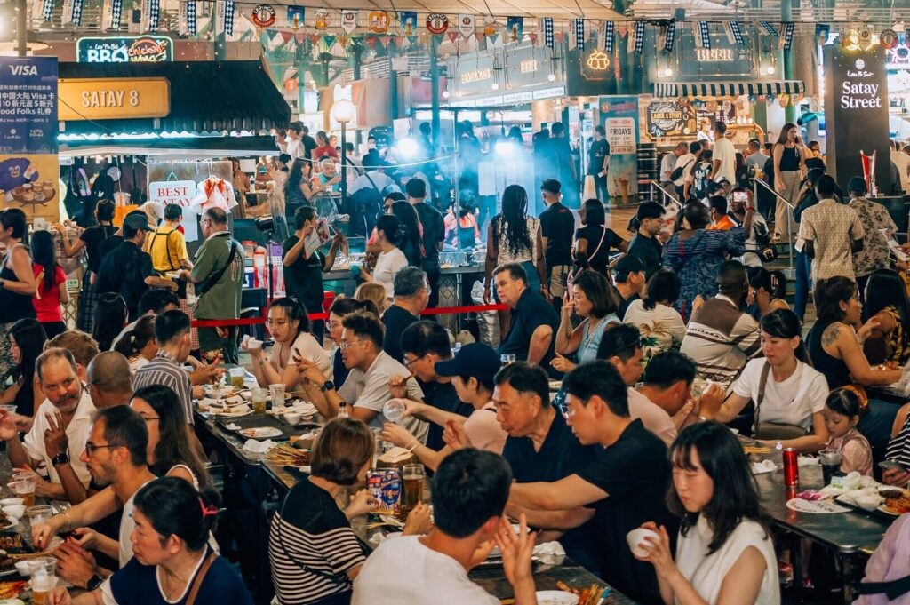 Crowded Singapore hawker dining scene with diverse people savoring meals and beverages in a vibrant atmosphere.
