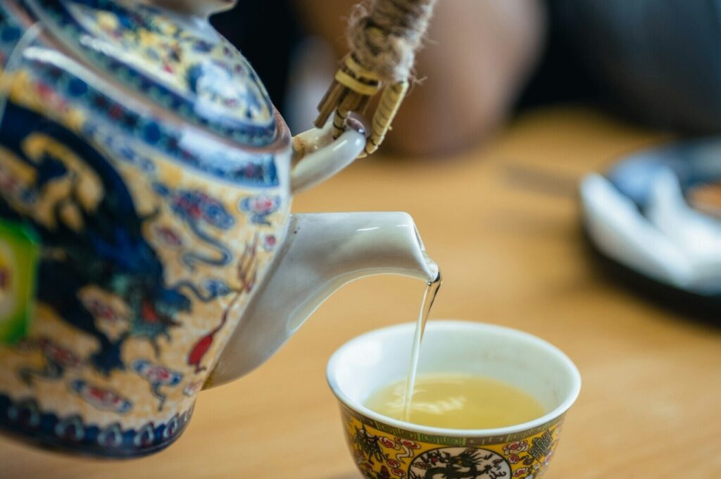 In a Chinese tea room, a person pours steaming tea into a delicate cup placed on a wooden table.