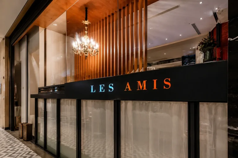 Les Amis restaurant exterior with illuminated sign and chandelier visible through glass