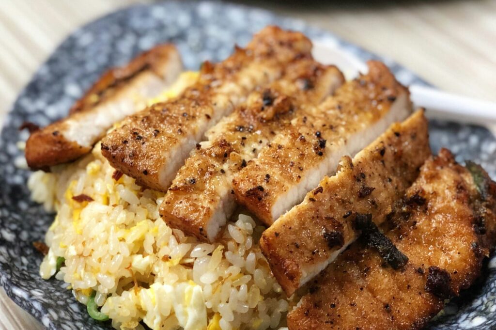 Grilled chicken slices on golden egg fried rice served on a blue speckled plate, creating a warm, appetizing, and inviting presentation.