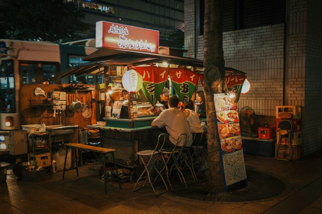 People enjoying food at a Singaporean hawker stand, surrounded by vibrant street food offerings.