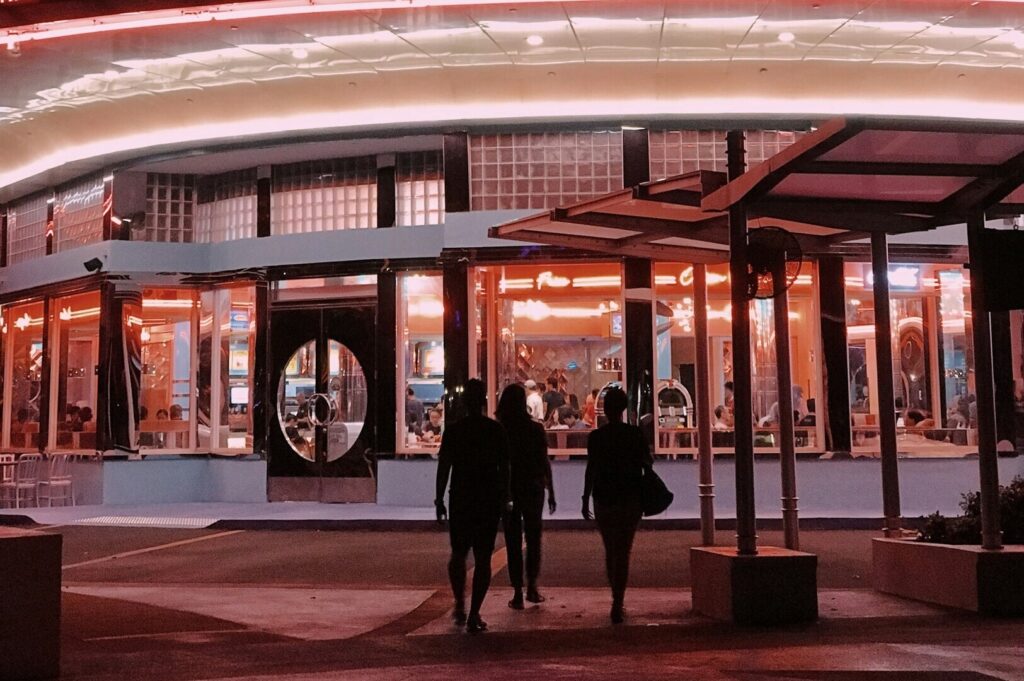 A group of people strolls in front of a neon-lit building showcasing 'Singapore Dining' in vibrant colors.