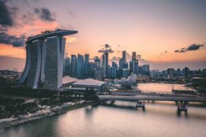 A stunning skyline of Singapore at sunset, featuring the iconic Marina Bay Sands, modern skyscrapers, and a calm waterfront reflecting the warm hues of the sky.