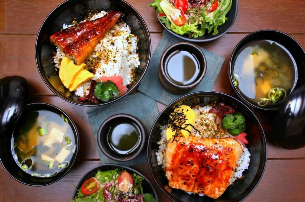 A dining table featuring an assortment of food bowls and rice, highlighting the culinary offerings of Singapore Izakaya.