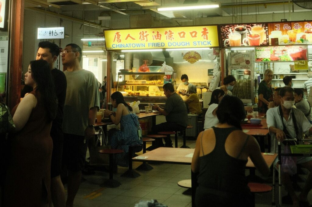 A lively scene of people savoring dishes at a Singaporean hawker, showcasing diverse culinary offerings in a communal setting.