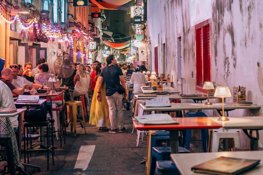 Outdoor dining setup in a narrow Singapore alley, with tables and chairs arranged for guests.