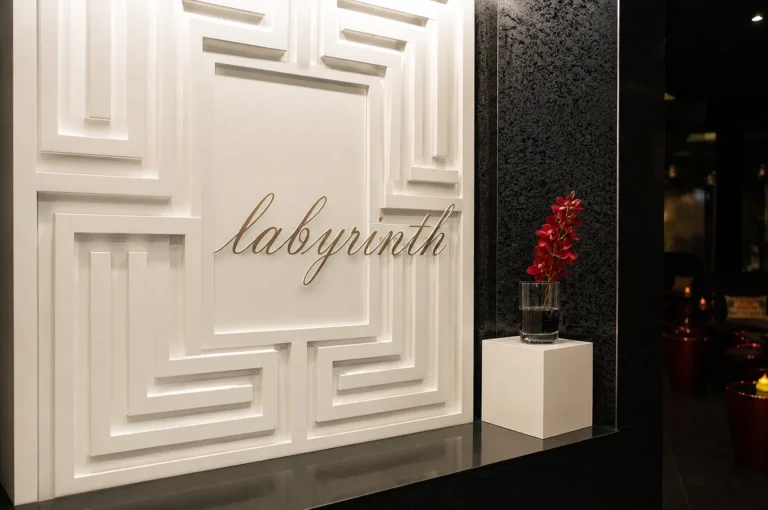 White geometric wall featuring gold "Labyrinth" script next to a red orchid display