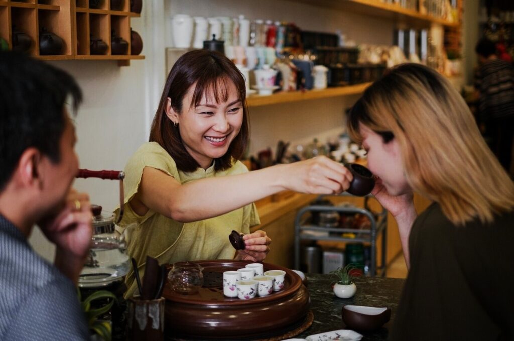 In Yixing Xuan Teahouse, a woman pours tea for two seated guests at a table on Tanjong Pagar Road.