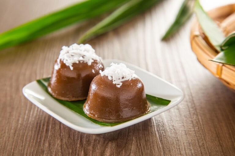 A white plate featuring two small Peranakan desserts garnished with coconut flakes.