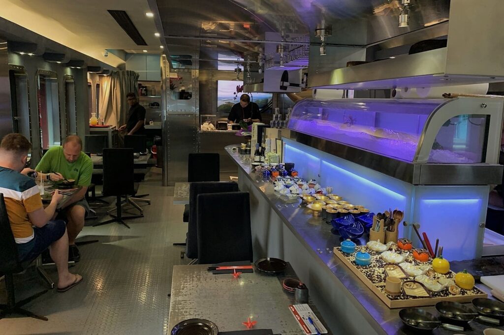 Inside Sushi Airways, Singapore, patrons are seated at tables, savoring sushi and beverages in a lively atmosphere.