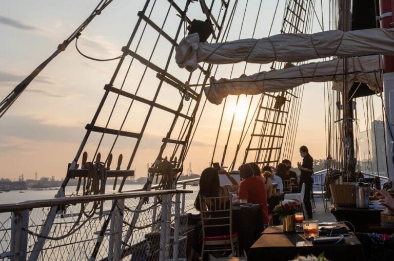 Guests are seated on the deck of the Royal Albratross, a tall ship in Singapore, surrounded by a beautiful maritime setting.
