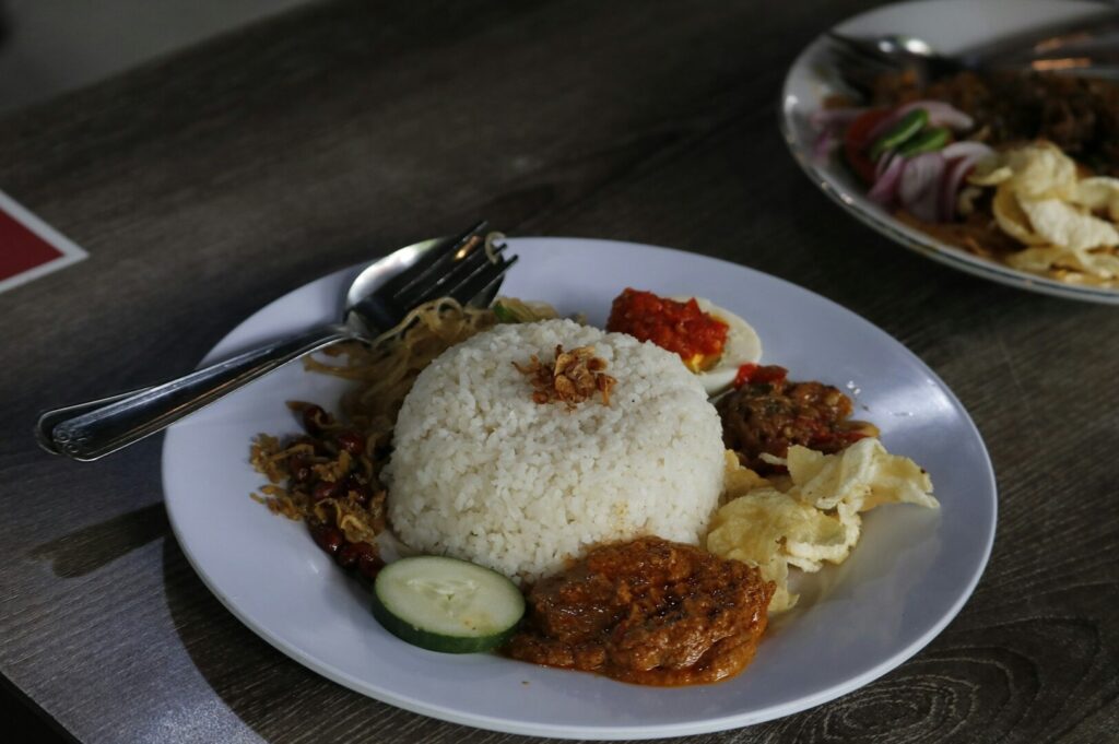 A plate of Nasi Lemak served on a table, featuring rice, sambal, fried egg, and cucumber slices.