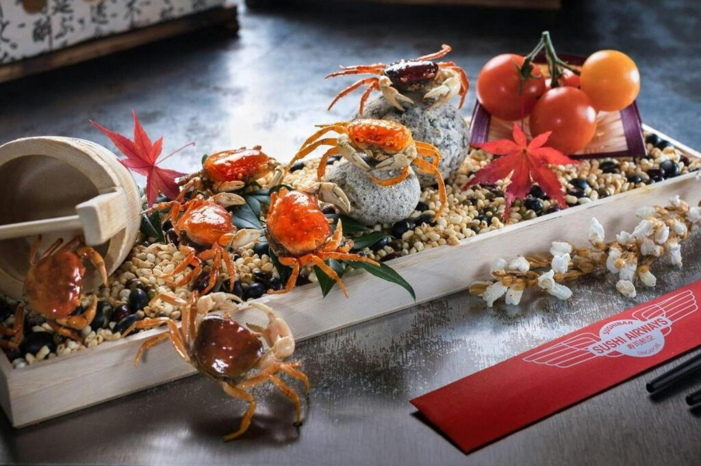 A tray featuring crabs, assorted vegetables, and various dishes from Sushi Airways Singapore.