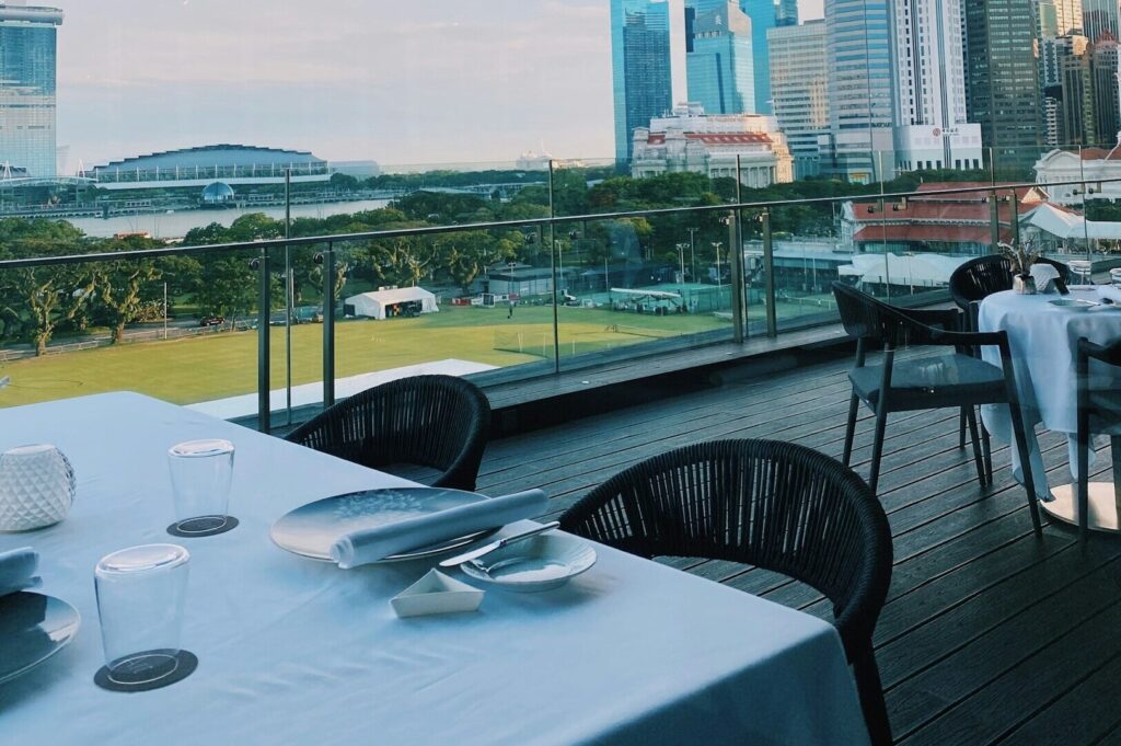 Elegant dining setup with a white tablecloth and chairs, overlooking the city from a restaurant in Singapore.