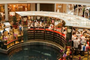 A bustling, curved tea shop in a mall features shelves of colorful teapots and tins. Customers and staff are busy. The atmosphere is lively and inviting.