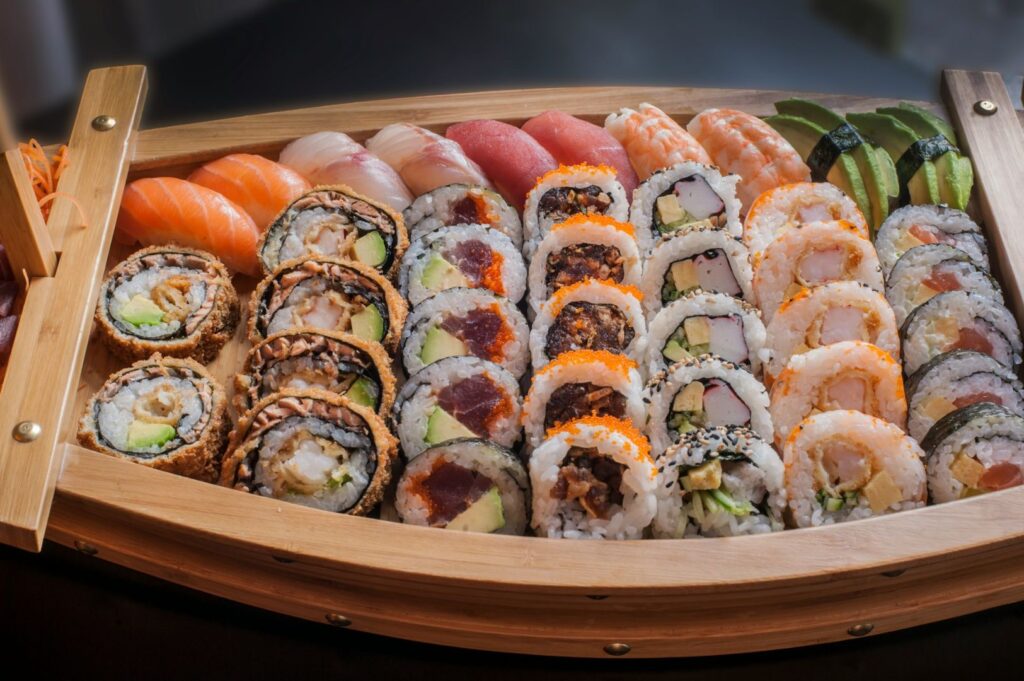 A wooden sushi boat display holding an assortment of sushi and sashimi, including nigiri, rolls with avocado and seafood. Vivid colors and fresh presentation.